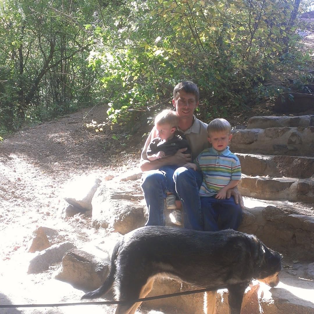 Family walking with a dog in a shallow forest stream.